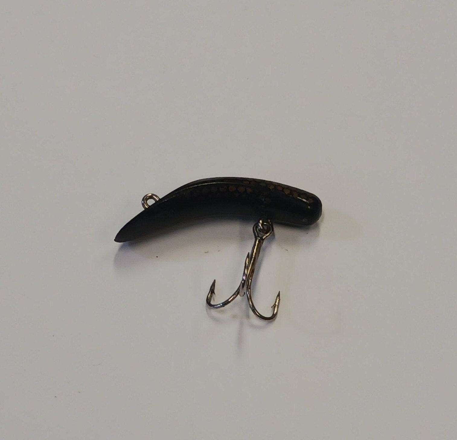Black fishing lure with a hook on a gray background